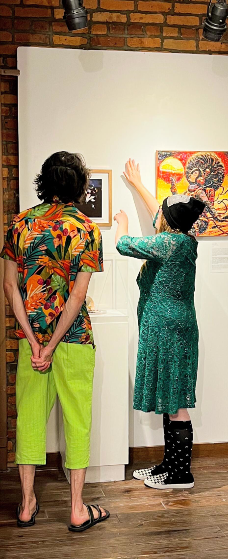 Two people facing a gallery wall while the person on the right explains the art hanging.
